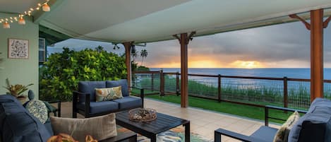 A covered outdoor seating area with a view of the ocean at sunset.