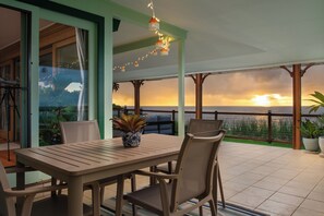 A patio with a table and chairs, overlooking a scenic view of the ocean at sunset. - Honoli‘i Sunrise House | 1BR/1BA | A More Better Home (Hilo)