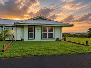 A small, single-story building with a green roof and white walls, featuring a sign that reads 'Welcome Guest Parking.' - Honoli‘i Sunrise House | 1BR/1BA | A More Better Home (Hilo)