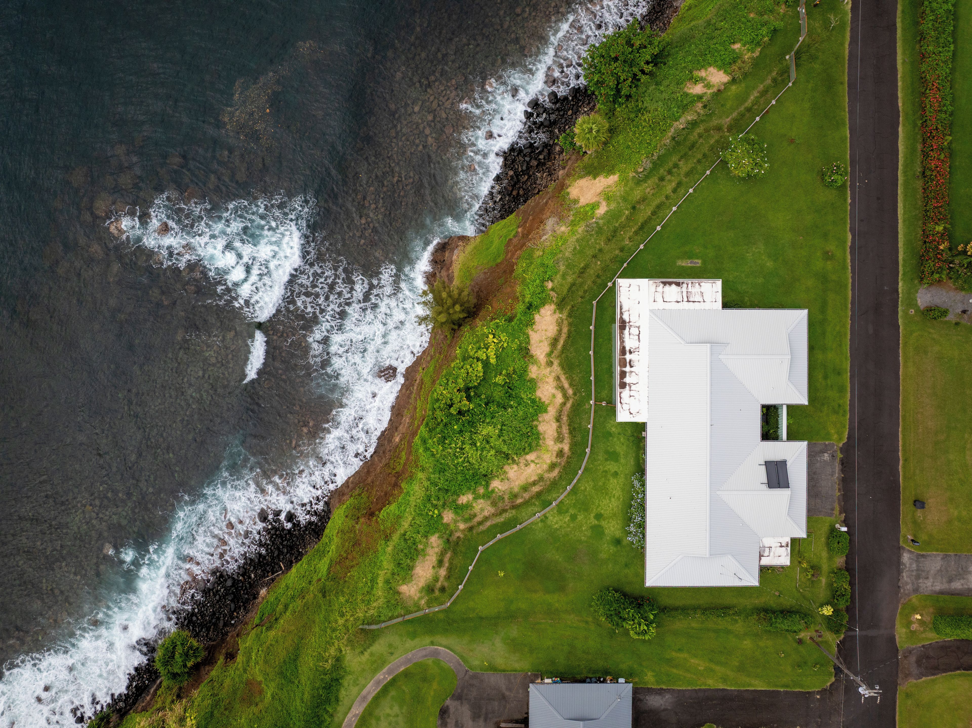 Vue aérienne d’une propriété située sur la côte, avec un grand bâtiment, une zone herbeuse et une route.