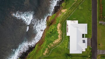 Luchtbeeld van een landgoed aan de kust, met een groot gebouw, een gazon en een weg.