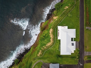 Luchtbeeld van een landgoed aan de kust, met een groot gebouw, een gazon en een weg.