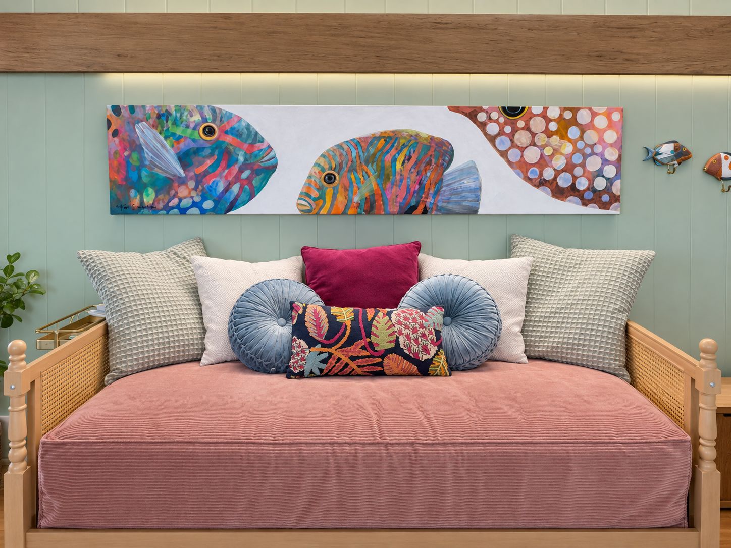 Un lit avec une couvre-lit rose, de nombreux oreillers et des œuvres d’art murales représentant des poissons aux couleurs vives.