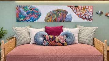 Un lit avec une couvre-lit rose, de nombreux oreillers et des œuvres d’art murales représentant des poissons aux couleurs vives.
