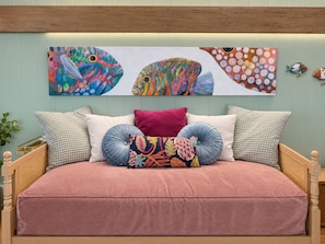 Een bed met een roze dekbedovertrek, meerdere kussens en wanddecoratie met kleurrijke vissen.