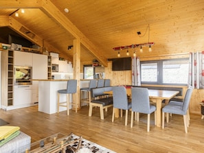 A wooden interior with a dining area, kitchen, and a TV mounted on the wall. - Premium Chalet #13 With Sauna & Swim Spa (Schladming)