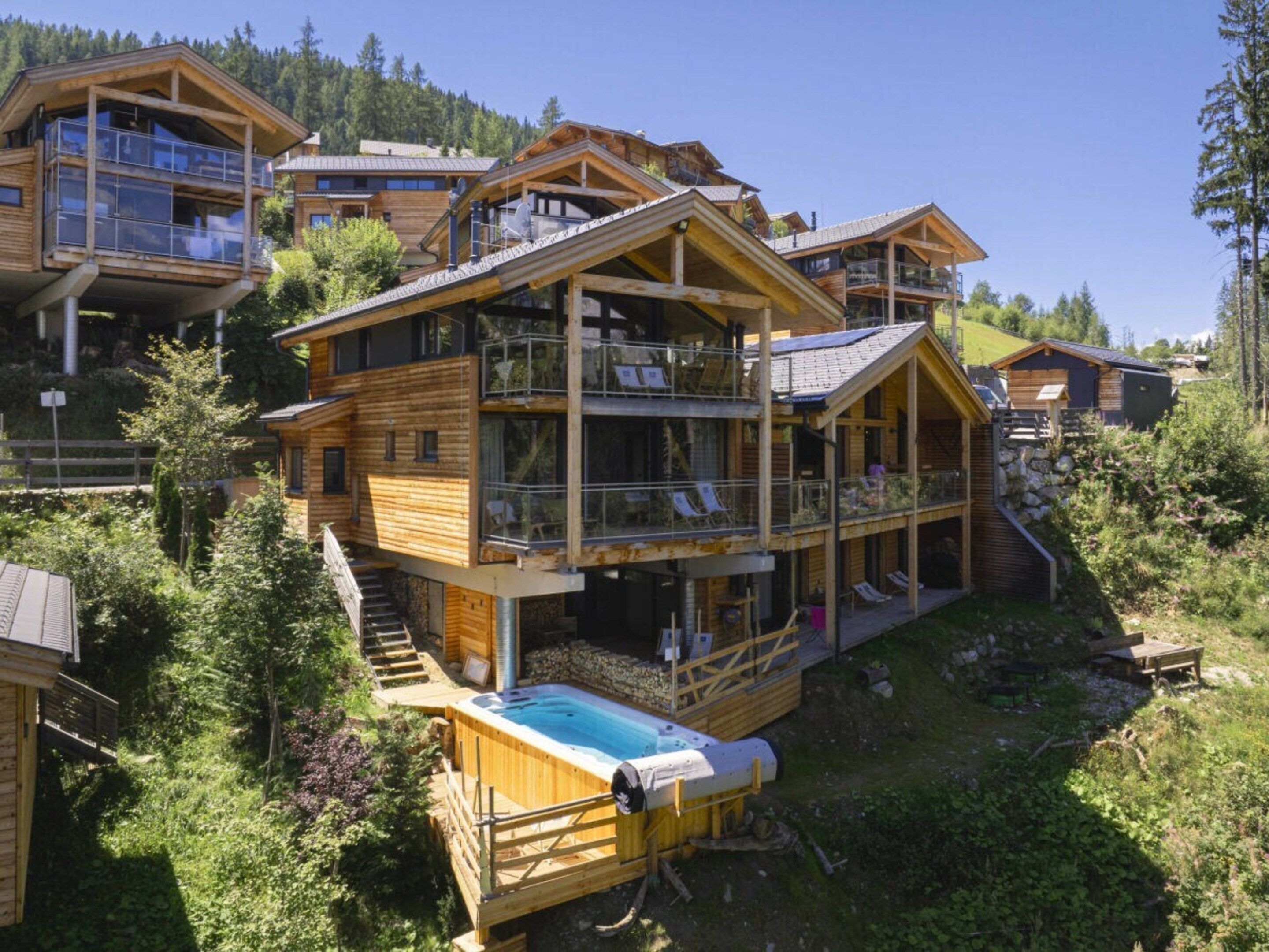 A wooden chalet with multiple balconies, a hot tub, and a view of the surrounding forest.