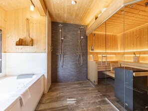 A modern bathroom with a wooden interior, a bathtub, a shower area, and a glass-enclosed sauna. - Premium Chalet #13 With Sauna & Swim Spa (Schladming)