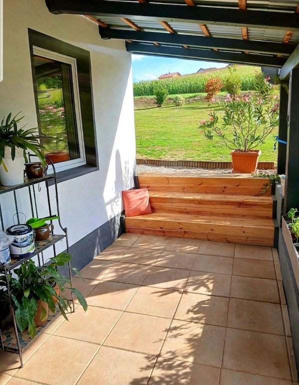 A covered patio area with a view of a green field and a building in the distance.