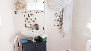 A bathroom with a sink, mirror, shower, and patterned floor tiles.