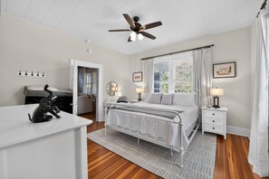 A bedroom with a bed, bedside tables, a desk, a ceiling fan, and a view of the outdoors through the window. - QCA House | 1 Mile to Bryant-Denny Stadium! (Tuscaloosa)
