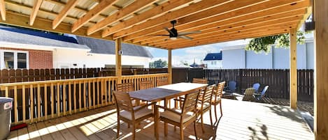 A wooden deck with a table and chairs, a ceiling fan, and a view of a house in the background.