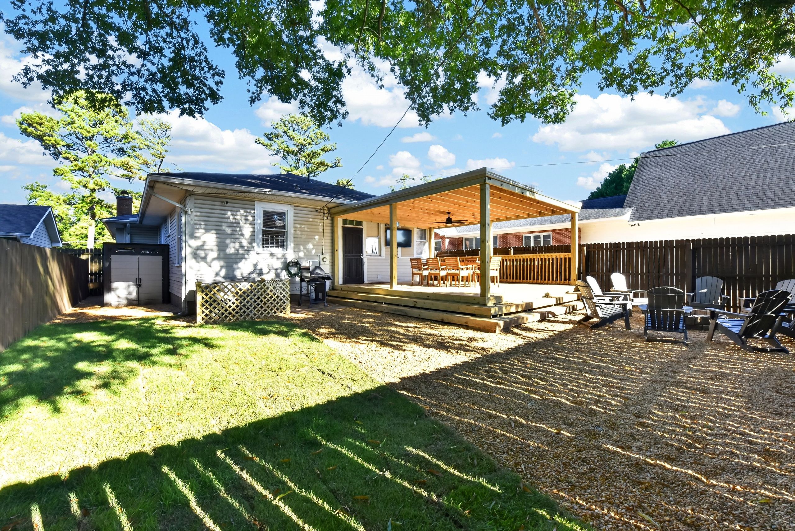 A residential backyard with a covered patio, a lawn, and a wooden deck.