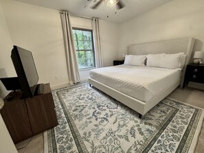 Een slaapkamer met een bed, een televisie, een nachtkastje, een lamp en een raam met gordijnen.
