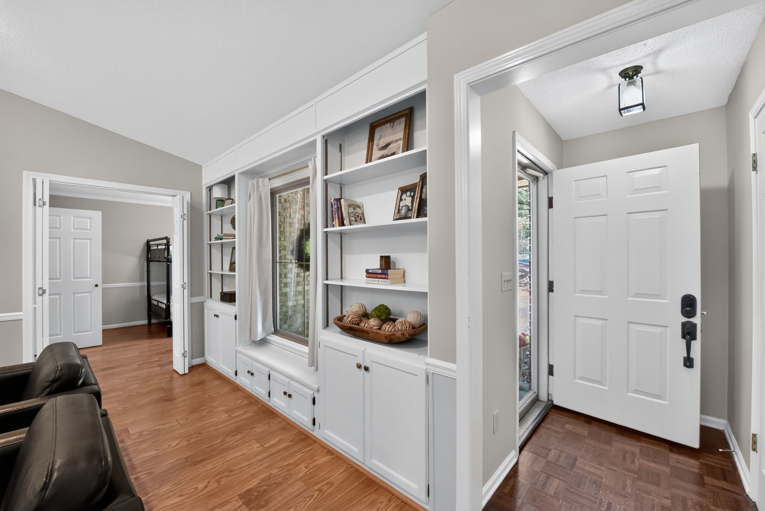 A spacious room with a built-in bookshelf, a seating area with a leather chair, and a door leading to another room.