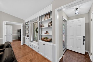 A spacious room with a built-in bookshelf, a seating area with a leather chair, and a door leading to another room.