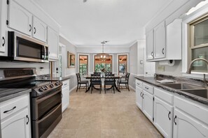A kitchen with white cabinetry, a built-in microwave, a stove, and a dining area with a table and chairs.