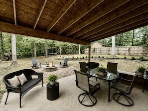 Een terras buiten met een houten plafond, een tafel met glazen blad en omliggende stoelen.