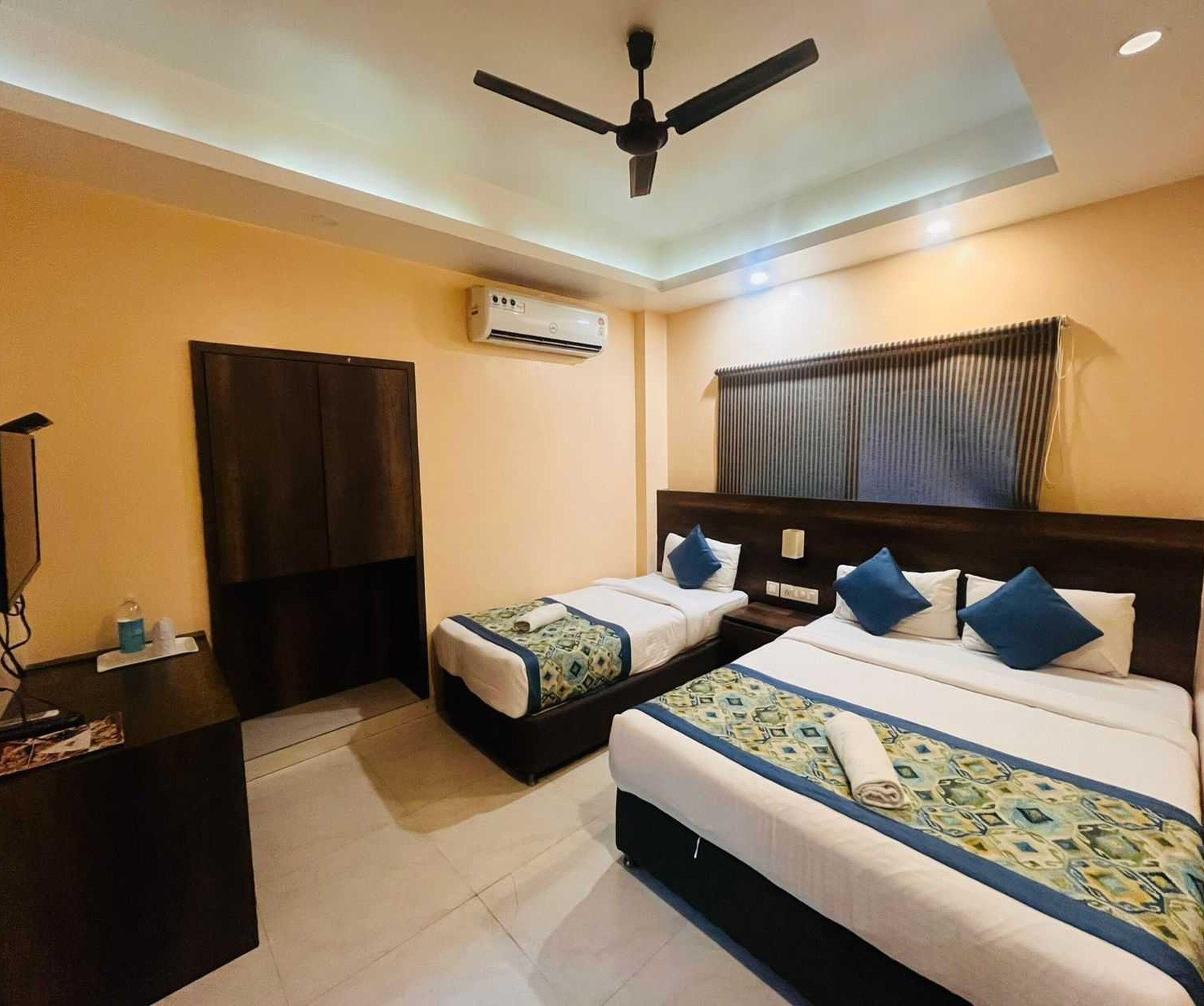 Une chambre d’hôtel avec deux lits, un ventilateur de plafond, un appareil de climatisation, une table de chevet et une fenêtre avec des stores.