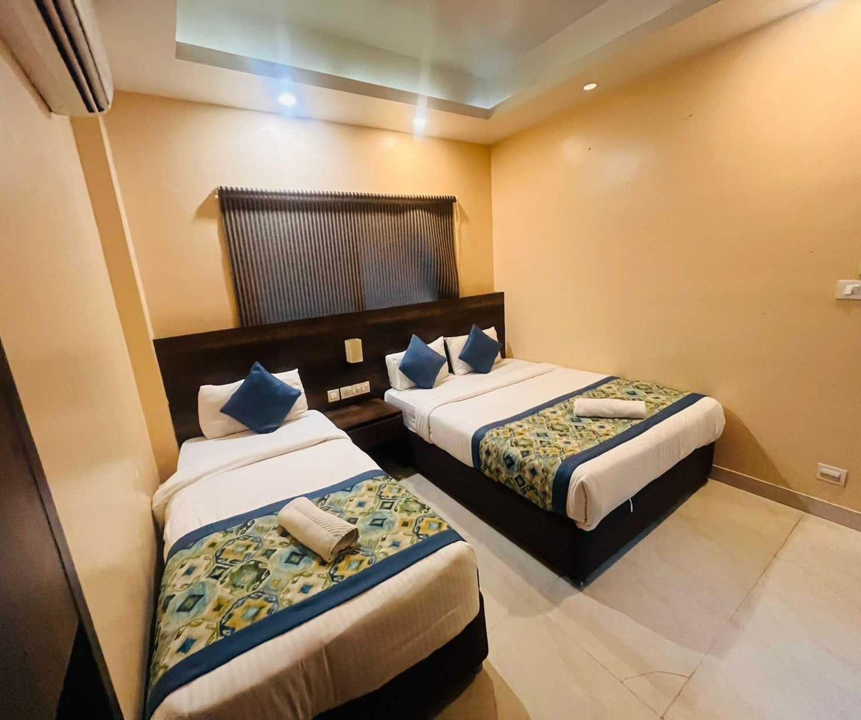 A hotel room with two beds, each with a headboard, a window with blinds, and a ceiling light.