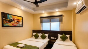 Habitación de hotel con dos camas individuales, ventilador de techo, aire acondicionado, ventana con persianas y un cuadro en la pared.