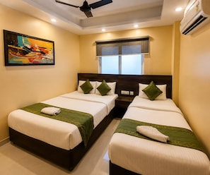Quarto de hotel com duas camas de solteiro, ventilador de teto, ar condicionado, janela com cortinas e um quadro na parede.