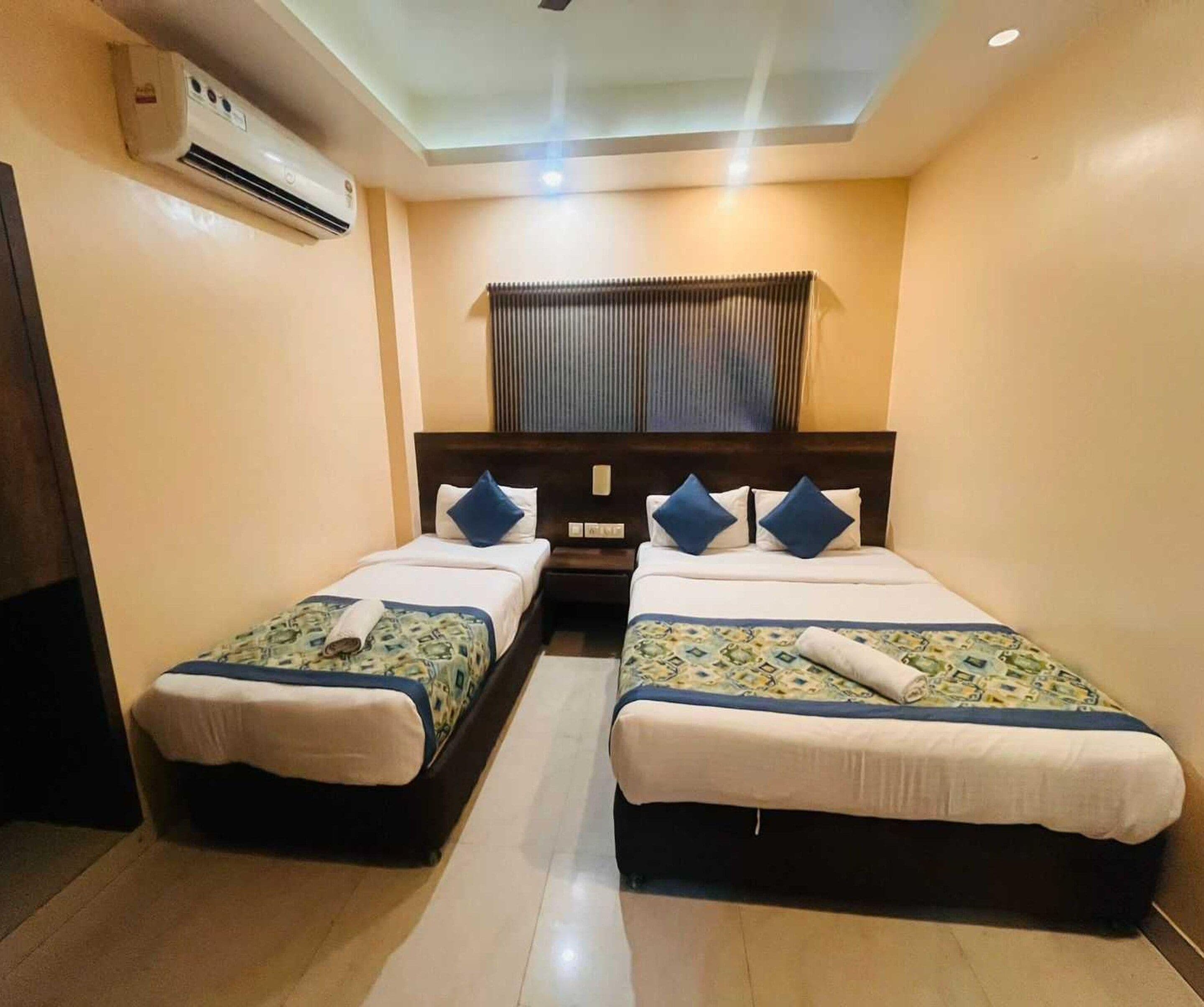 Una habitación de hotel con dos camas, ventilador de techo, unidad de aire acondicionado y ventana con persianas.