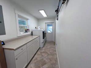 A narrow kitchen with white cabinets, a built-in washer and dryer, a window, and a door leading to a balcony. - Luxury Gulf-View Home with Private Pool (Mexico Beach)