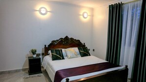 Un dormitorio con una cama de madera, dos lámparas de noche, una mesita de noche, una planta en maceta y una ventana con cortinas.