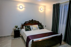 Ein Schlafzimmer mit einem hölzernen Bett, zwei Nachttischlampen, einem Nachttisch, einer Topfpflanze und einem Fenster mit Vorhängen.