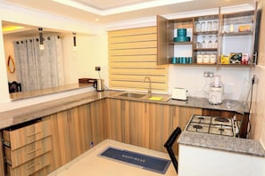 A kitchen with wooden cabinets, a built-in stove, a coffee maker, and a shelf with kitchenware.