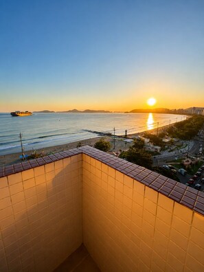 A view from a tiled balcony overlooking a beach with a sunset, a cargo ship, and a cityscape in the distance. - Oceanfront - Panoramic View, Cinematic Sunset (Santos)