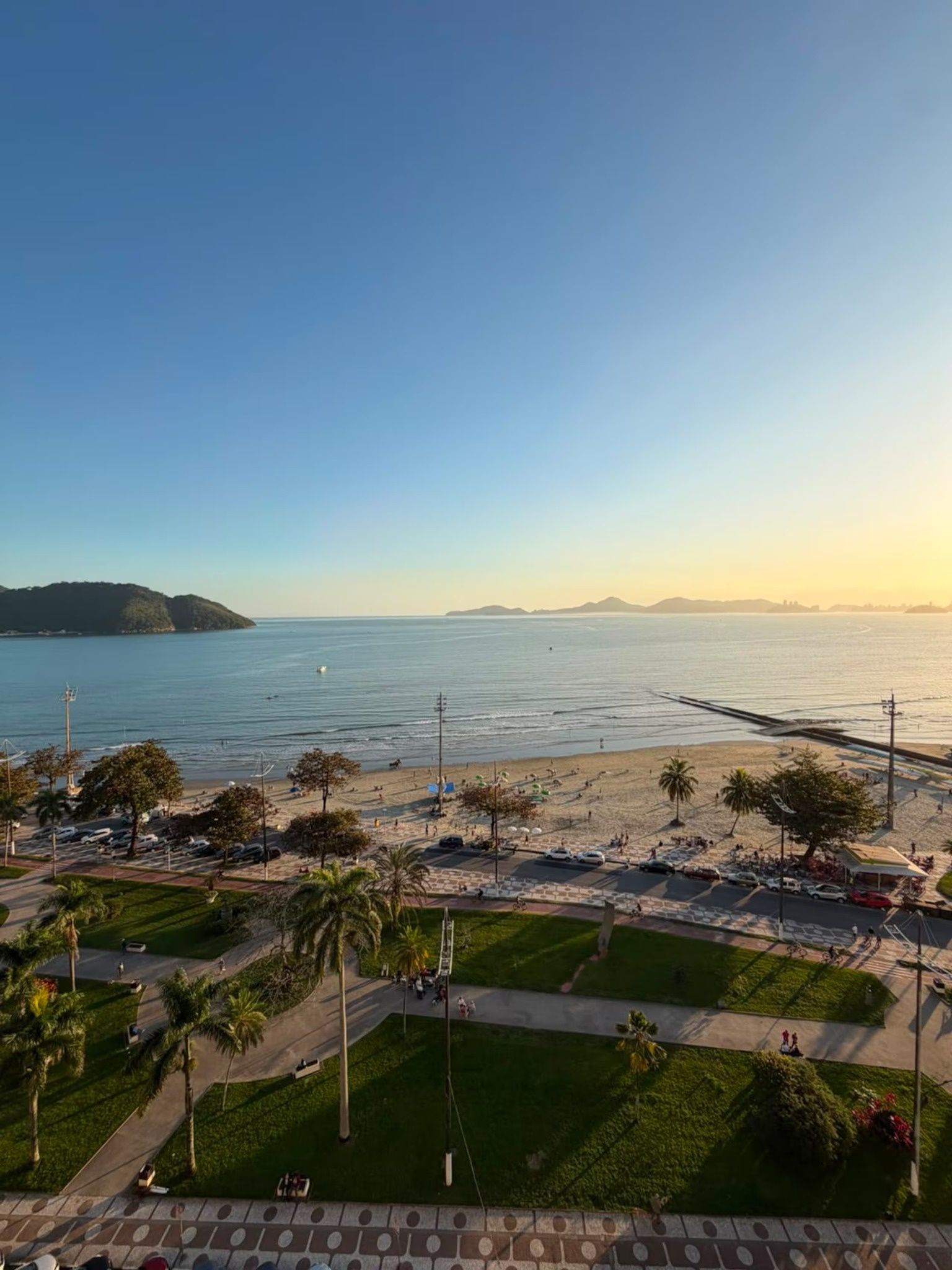 A coastal view with a beach, promenade, and distant mountains.