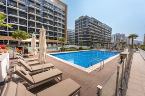 Ein Dachpool mit Liegestühlen und Sonnenschirmen, umgeben von Hochhäusern.