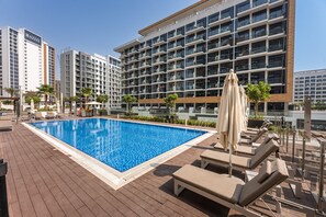 Ein Pool auf dem Dach mit Liegestühlen und Sonnenschirmen, umgeben von Hochhäusern.