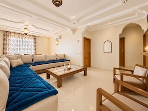 A spacious living room with a sofa set, a coffee table, and a wooden chair. - Amazigha - Appartement 3 chambres à 200 m de la plage (essaouira)