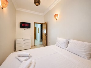 Ett hotellrum med en säng, en tv som visar ”NETFLIX”, en garderob och en dörr som leder till ett annat rum.