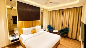Habitación de hotel con una cama grande, mesitas de noche, un escritorio, dos sillas, un ventilador de techo y un amplio ventanal con cortinas.