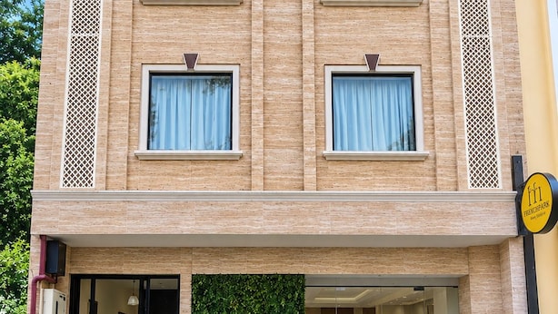 Un hotel de varios pisos con fachada de ladrillo, ventanas grandes con cortinas y una entrada bien cuidada con plantas en macetas.