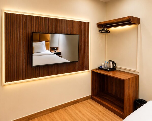A hotel room with a bed, a bedside table with a mirror, and a wall-mounted TV. - The Benchmark Hotel (Indore)