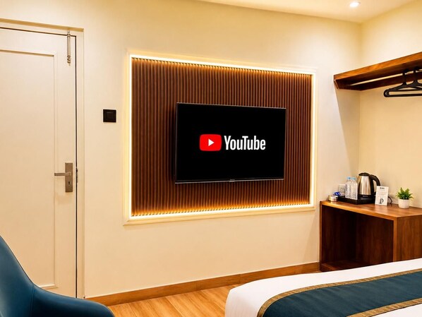 Habitación de hotel con cama, televisor montado en la pared, escritorio de madera y una silla azul.