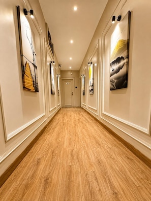 Un pasillo con piso de madera, obras de arte en la pared e iluminación empotrada.