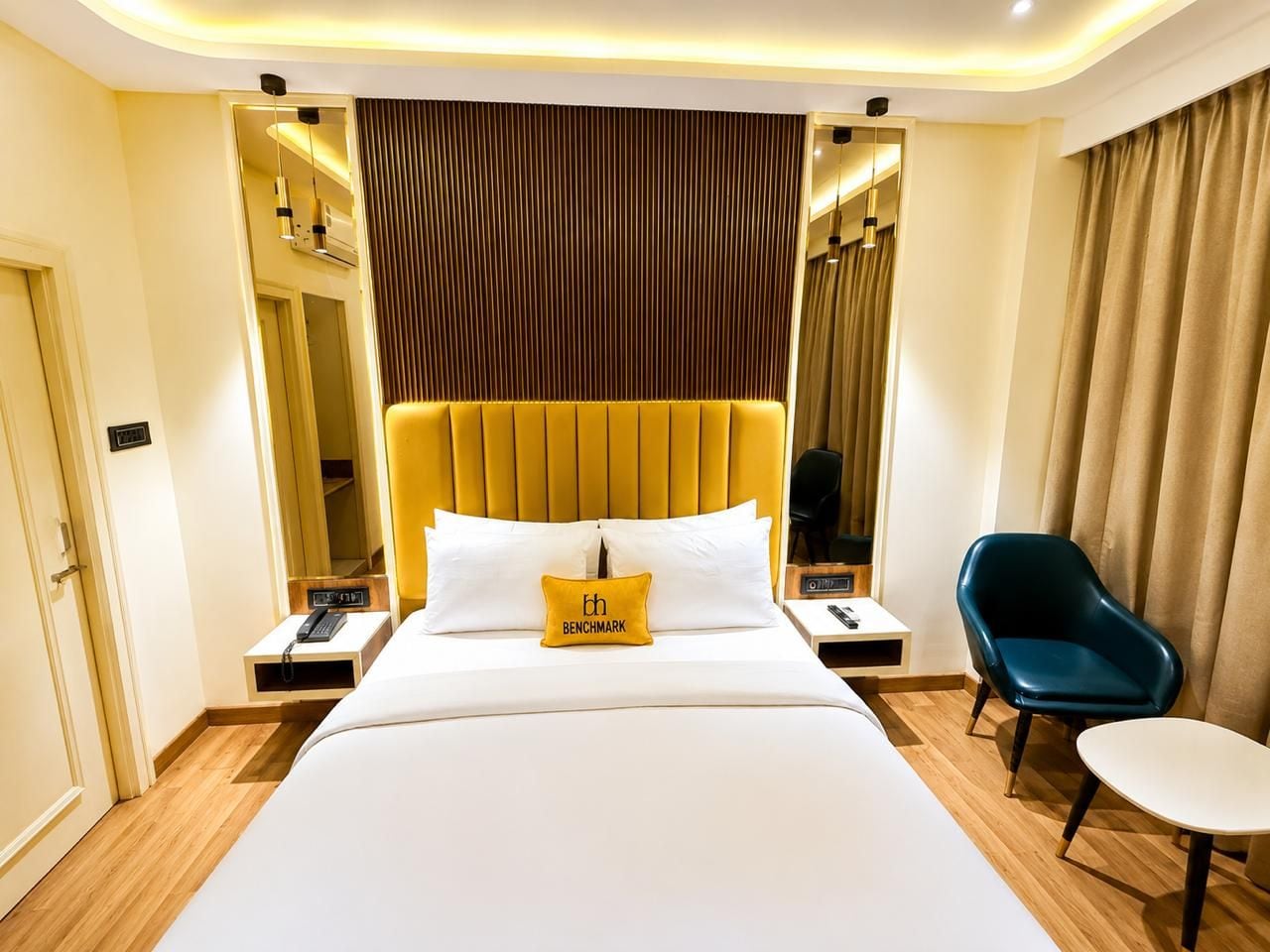 A hotel room with a large bed, a bedside table with a telephone, a chair, and a mirror.