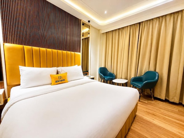 A hotel room with a large bed, two chairs, a small table, and a wooden floor.
