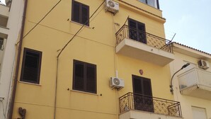 A multi-story building with balconies, air conditioning units, and a visible door number. - 5 minutes from the square and the airport (Terrasini)