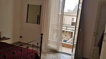 Ein Schlafzimmer mit einem Bett, einem Spiegel, einer Tür zu einem Balkon und Blick auf Gebäude.