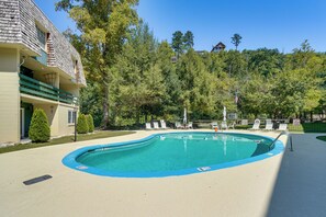 A swimming pool with lounge chairs, surrounded by trees and a building with a sloped roof. - Cozy Updated Gatlinburg Condo Minutes to Downtown (Gatlinburg)