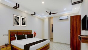 A modern hotel room with a large bed, a bedside table, a wall-mounted TV, and a ceiling fan. - Deluxe Room Saibala Lodge (Vellore)