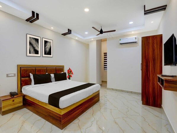 A modern hotel room with a large bed, a bedside table, a wall-mounted TV, and a ceiling fan.