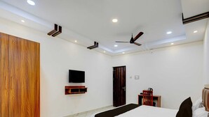A modern bedroom with a bed, a TV, a wardrobe, and a ceiling fan. - Deluxe Room Saibala Lodge (Vellore)